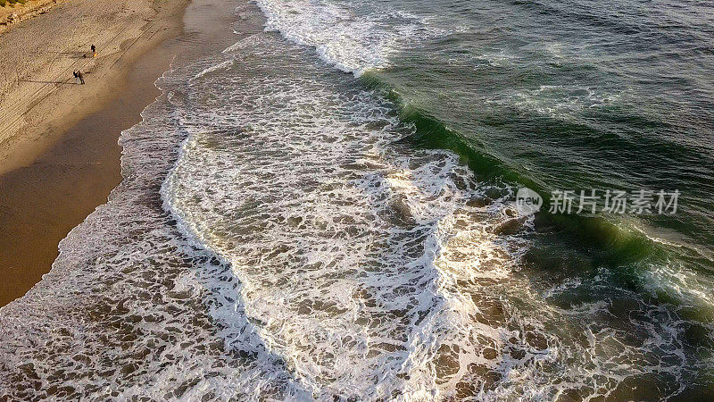 海滩和海浪的近景日落附近的国际边界墙在Playas Tijuana，墨西哥